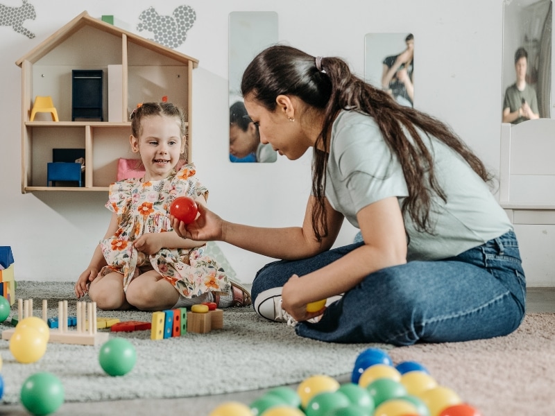 Educator guiding child with coloured toys during a school readiness test session.